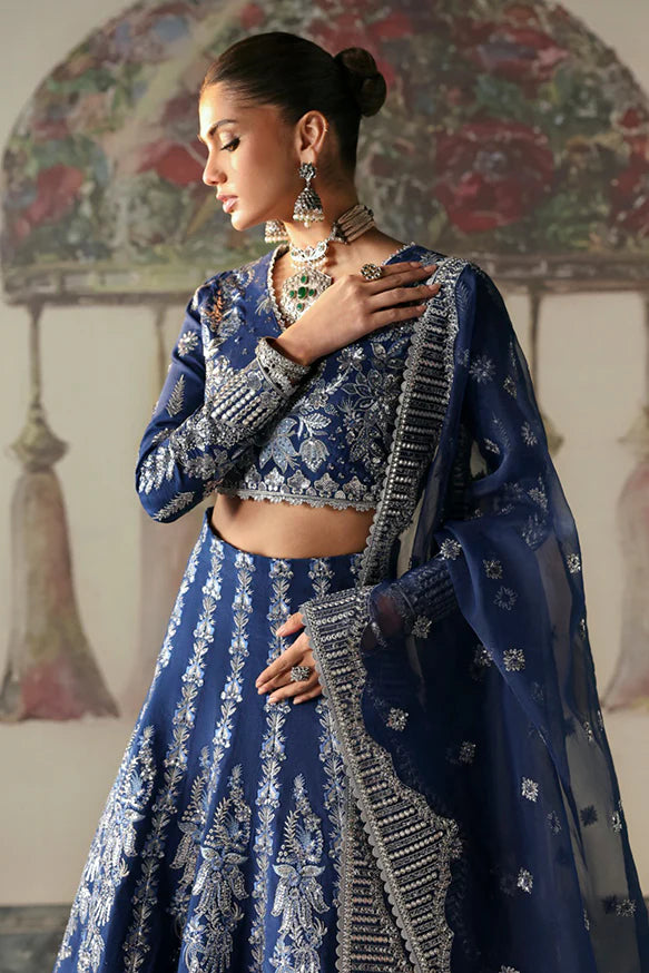 Nazli – Blue embroidered raw silk lehnga choli with sequins, tilla, and silver panni, paired with an embroidered organza dupatta.

